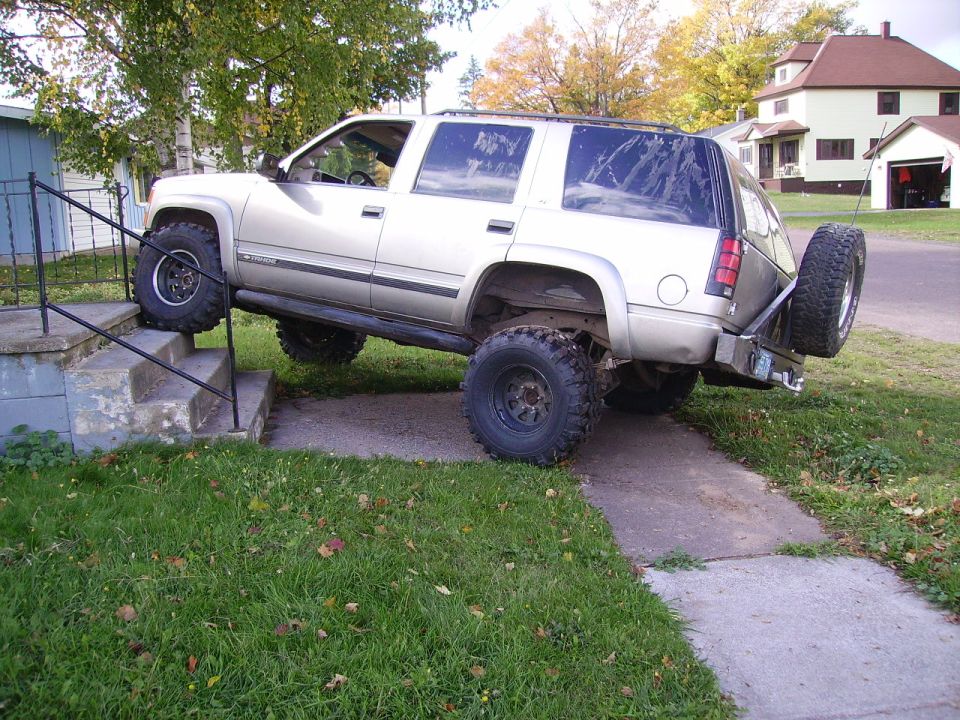 Silver SUV with large tires driving up concrete stairs next to a house