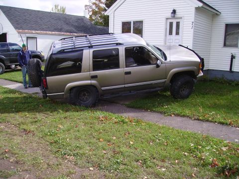 2000 Chevrolet Tahoe - A gold Chevrolet Tahoe is parked on the grass, partially on a sidewalk, next to a white house.