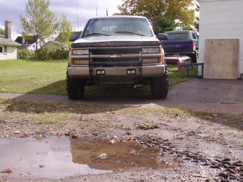 2000 Chevrolet Tahoe - This pickup truck, likely from the mid-1990s, is parked in a driveway with a puddle in the foreground and another vehicle in the background.