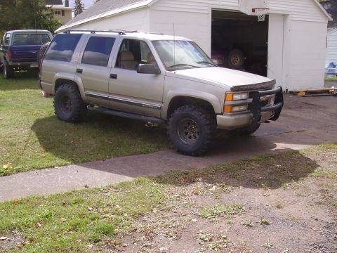 2000 Chevrolet Tahoe - Gold Chevrolet Tahoe SUV with off-road tires parked in front of a garage. Another truck is visible in the background.