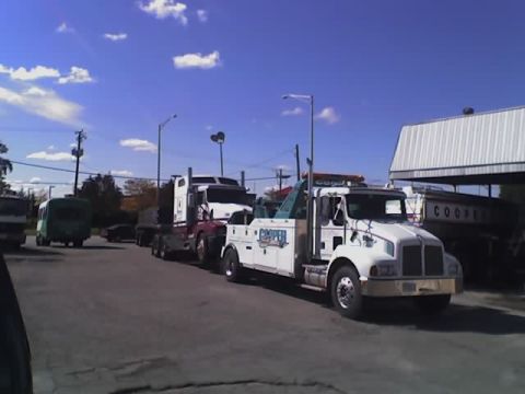 1992 Ford Bronco - A tow truck is preparing to haul a semi-trailer truck under a blue sky.