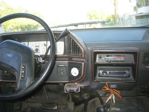 1990 Ford Bronco - Interior view of a Ford truck dash with woodgrain trim, an aftermarket double-stack stereo and a small aftermarket gauge.