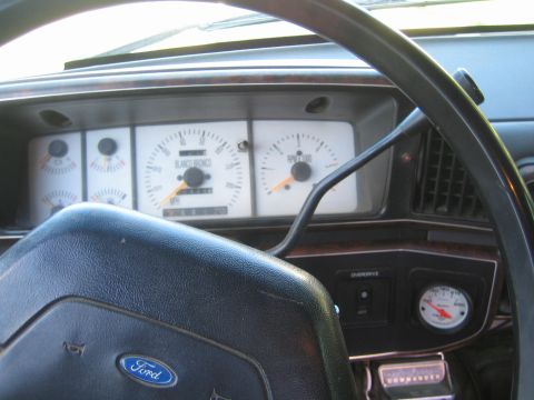 1990 Ford Bronco - View through a Ford steering wheel of a Bronco instrument cluster with tachometer, gauges and an aftermarket gauge below.
