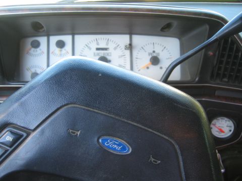 1990 Ford Bronco - Close-up of a Ford steering wheel hub in front of a Bronco instrument cluster with an aftermarket gauge to the right.