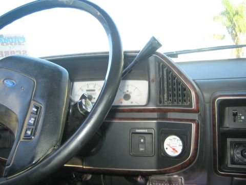 1990 Ford Bronco - Interior dashboard view showing a Ford steering wheel, analog gauge cluster, woodgrain trim panel and an overdrive on/off switch.