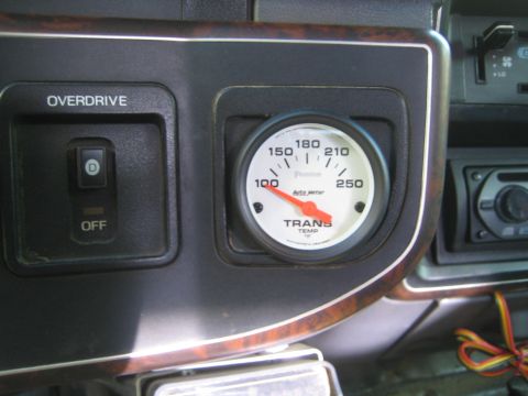 1990 Ford Bronco - Auto Meter Phantom trans-temp gauge reading 100-250 degrees mounted in a woodgrain dash next to an overdrive switch.