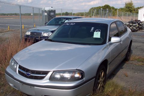 1991 Ford LTD Crown Victoria - Two sedans are parked in an outdoor lot with a portable toilet and stacked items in the background.