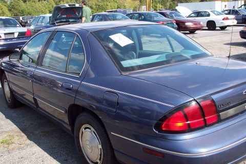 1991 Ford LTD Crown Victoria - A dark blue sedan is parked in a lot with other vehicles, some with hoods or trunks open.