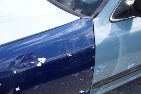 1991 Ford LTD Crown Victoria - Close-up of a damaged blue car door, showing deep scratches and areas where the paint is peeling off.