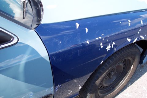 1991 Ford LTD Crown Victoria - The side panel of a car shows damage with peeling paint and scuff marks.