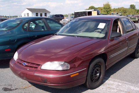 1991 Ford LTD Crown Victoria - Two sedans are parked in an outdoor lot with a small building in the background.