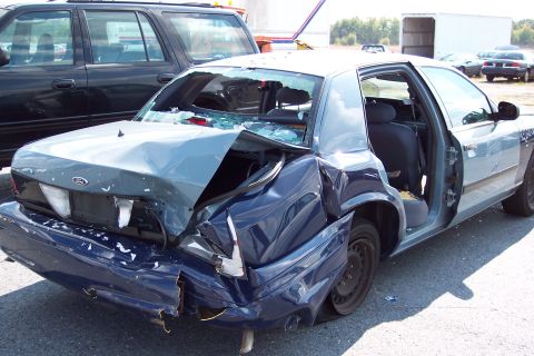 1991 Ford LTD Crown Victoria - A heavily damaged Ford Crown Victoria sits in a lot, its rear end crushed inwards.
