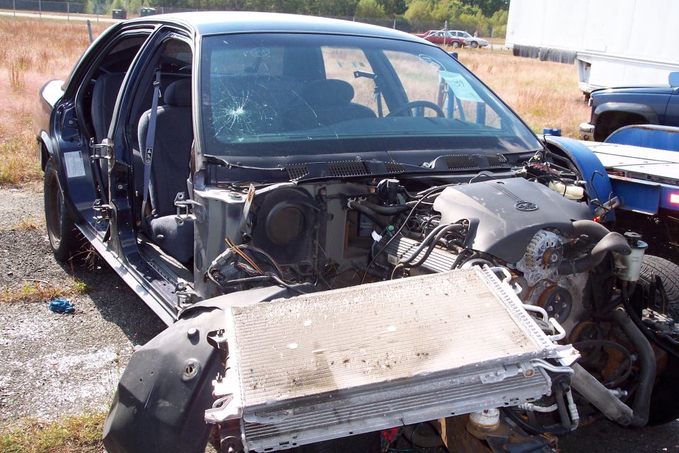 Damaged sedan with front end removed, showing engine and radiator. Windshield is cracked