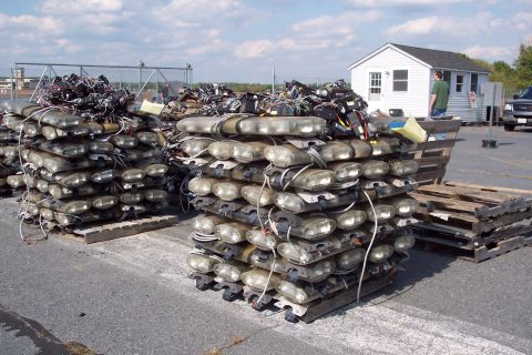 1991 Ford LTD Crown Victoria - Multiple stacks of police light bars are organized on wooden pallets in an outdoor lot.