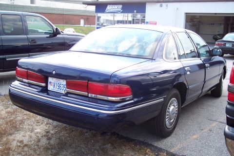 1991 Ford LTD Crown Victoria - A dark blue sedan is parked outdoors, with a pickup truck to its left and another vehicle to its right.