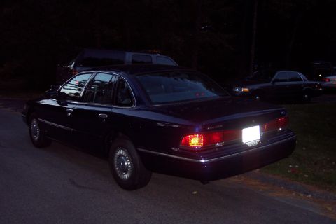 1991 Ford LTD Crown Victoria - A dark sedan is parked on the side of a road at dusk, with another vehicle visible in the background.