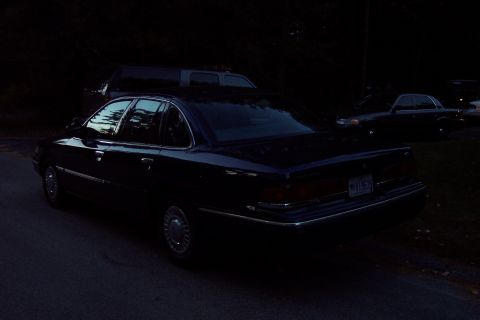 1991 Ford LTD Crown Victoria - A dark sedan is parked on the side of the road, with another vehicle visible in the background.