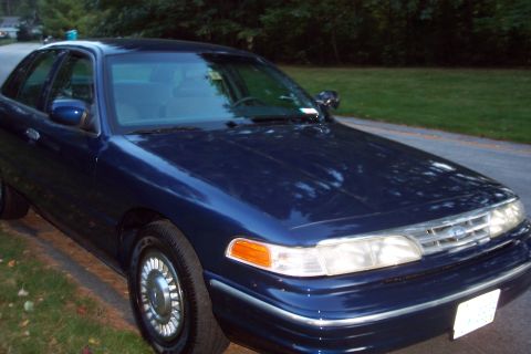 1991 Ford LTD Crown Victoria - A dark blue sedan is parked on the side of a road, with trees in the background.