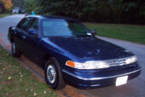 1991 Ford LTD Crown Victoria - A dark blue 1991 Ford Crown Victoria LTD sedan is parked on the side of a road, with trees and houses in the background.