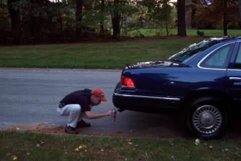 1991 Ford LTD Crown Victoria - A man sprays the exhaust pipe of a blue 1991 Ford Crown Victoria LTD parked on the side of the road.