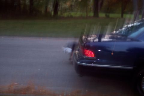 1991 Ford LTD Crown Victoria - Rear view of a dark sedan with a red taillight illuminated, parked on the side of a road.