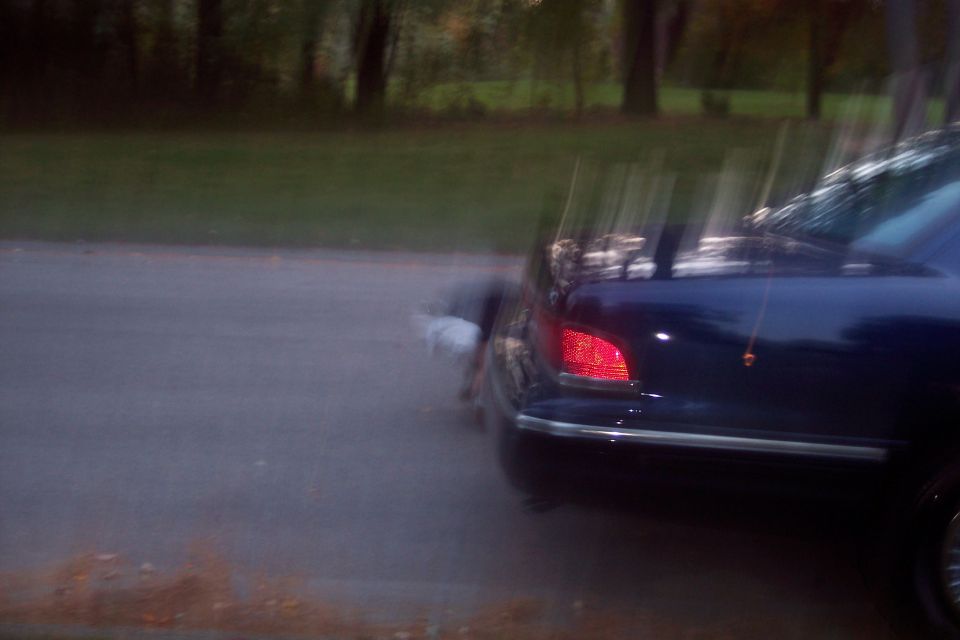 Rear view of a dark sedan with a red taillight illuminated, parked on the side of a road