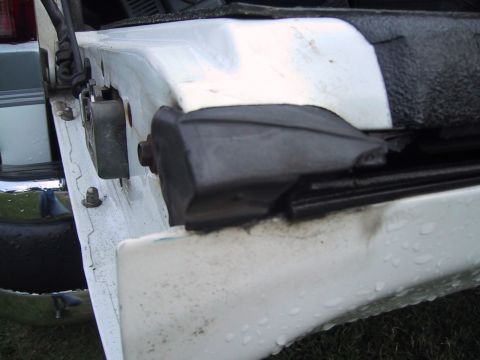 1994 Ford Bronco - Close-up of an open white door on a truck, shot down the leading edge to show the door latch/striker area, a black rubber wedge bumper stop…