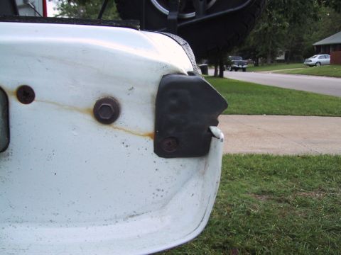 1994 Ford Bronco - Close-up of a white vehicle's rear corner, showing a damaged black trim piece and rusty hardware.
