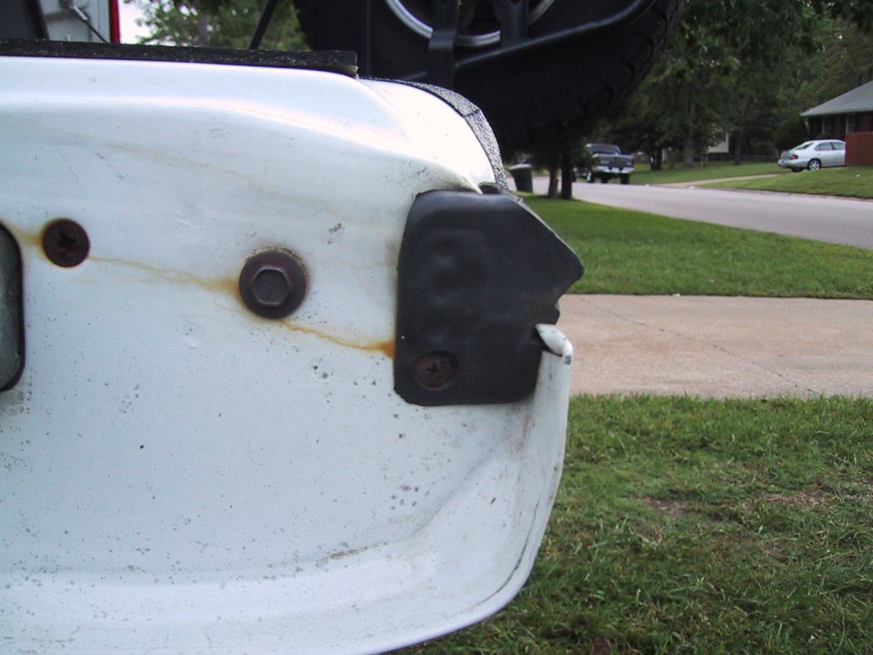 White tailgate corner with black plastic trim and rusty bolts