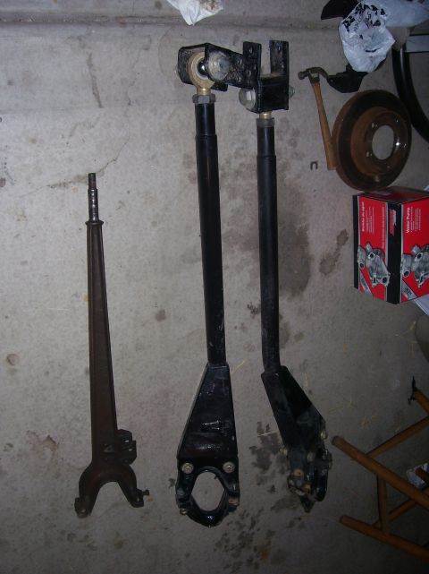 1984 Ford Bronco - Various suspension components are laid out on a concrete surface, including a long, thin part and two thicker, adjustable arms.