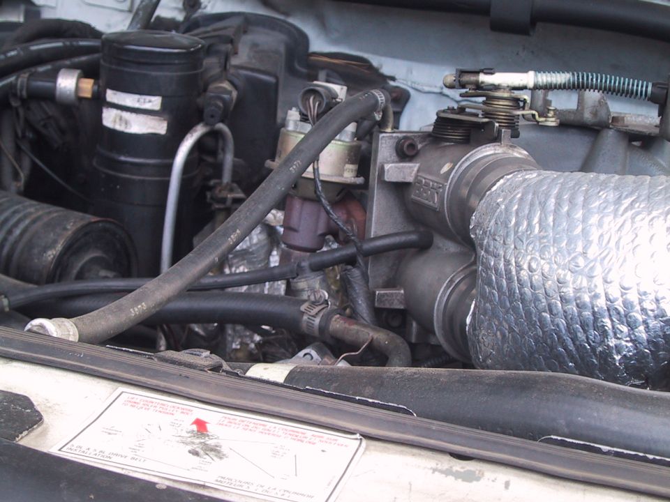Engine bay close-up of throttle body, linkage and heat-wrapped intake tube