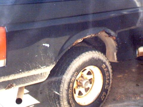1989 Ford Bronco - Close-up of a vehicle's rear wheel well showing rust and a tire with visible lettering.