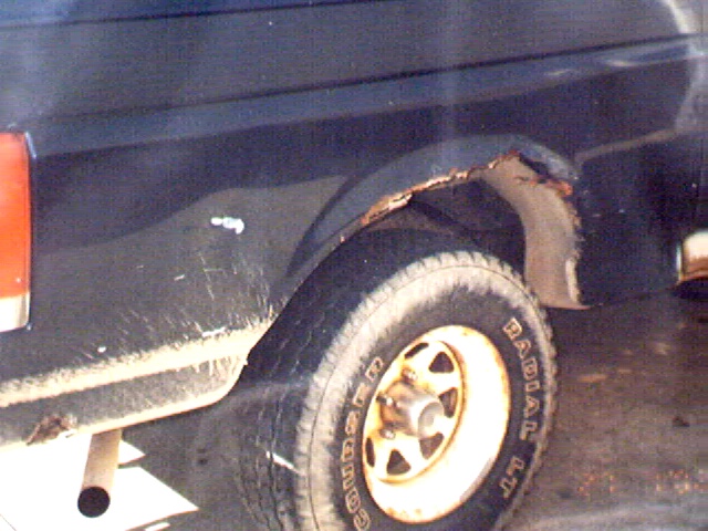 Rusted-through rear wheel arch on dark truck with Goodyear Wrangler tire and white wheel