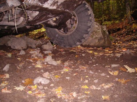 2000 Chevrolet Tahoe - The vehicle's undercarriage and tire are visible, stuck on rocks in a wooded area with fallen leaves.