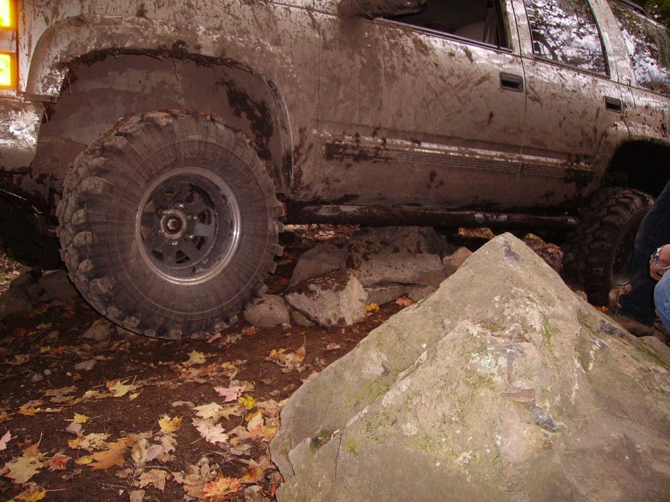 Mud-covered 2000 Chevrolet Tahoe driving over large rocks on a trail