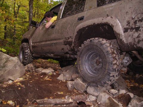 2000 Chevrolet Tahoe - SUV off-roading on a difficult rocky path with trees in the background.