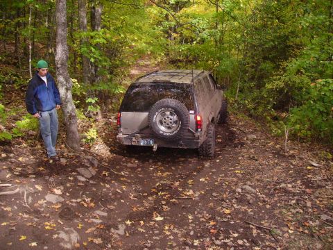 2000 Chevrolet Tahoe - An SUV navigates a muddy, leaf-covered trail through a forest.