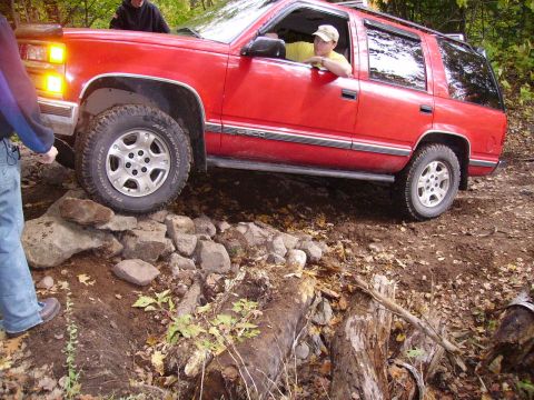 2000 Chevrolet Tahoe - A red Chevrolet Tahoe navigates a challenging off-road course with rocky terrain and fallen trees.