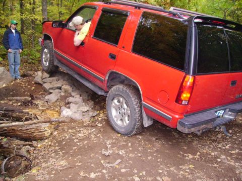 2000 Chevrolet Tahoe - A red SUV navigates a challenging rocky terrain, with a person observing from the side.