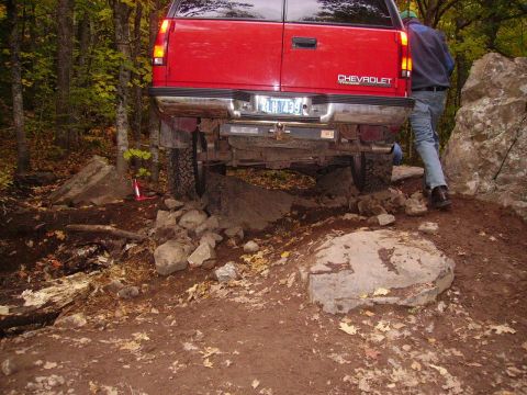 2000 Chevrolet Tahoe - A red Chevrolet SUV is shown from the rear, maneuvering over rocks and dirt on a wooded trail.