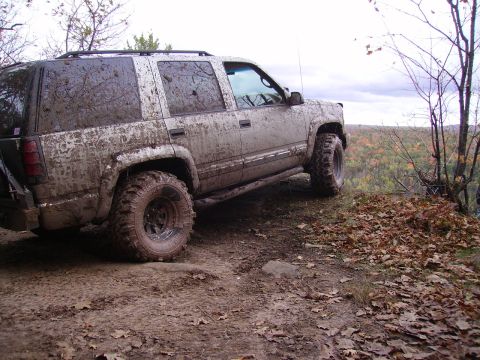 2000 Chevrolet Tahoe - This heavily mud-splattered SUV is parked precariously close to the edge of a cliff, overlooking a dense forest.