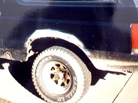 1989 Ford Bronco - The rear wheel well of a black 1989 Ford Bronco exhibits significant rust damage.