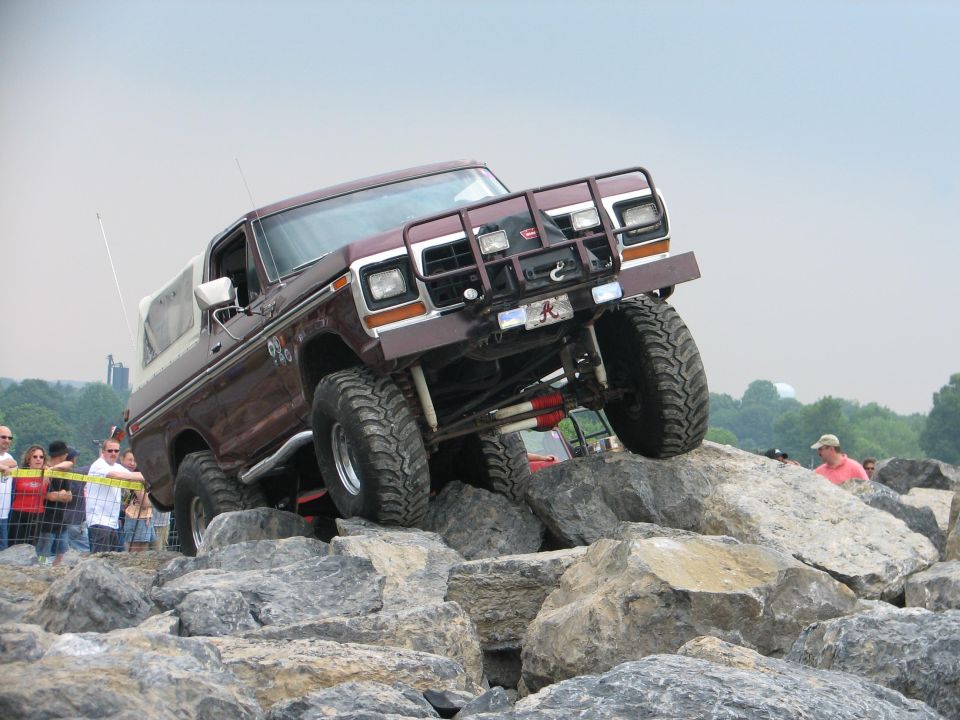 Brown 1978 Ford Bronco climbing large rocks, modified with off-road tires and a brush guard