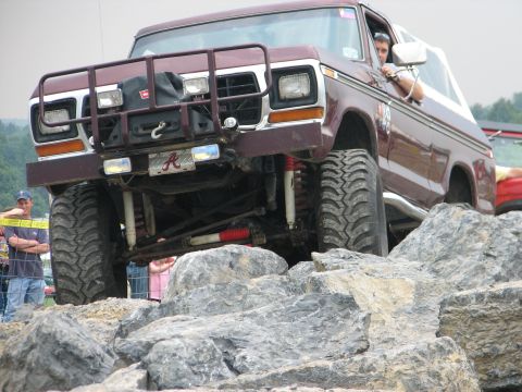 1992 Ford Bronco - This modified Ford Bronco is navigating a challenging rocky terrain, with spectators watching.