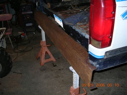 1991 Ford F-150 - A wooden plank is temporarily placed on jack stands in front of the rear bumper of a truck, possibly for repair or modification.