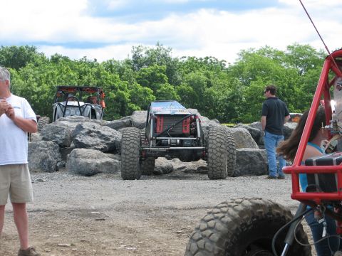 1992 Ford Bronco - A custom off-road buggy is seen from the rear, positioned amongst large rocks with other vehicles present.