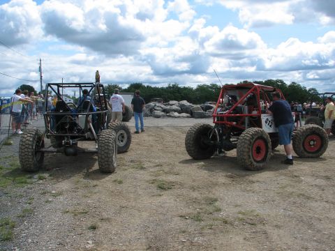 1992 Ford Bronco - Two custom-built off-road vehicles are parked side-by-side on a gravelly surface under a cloudy sky.