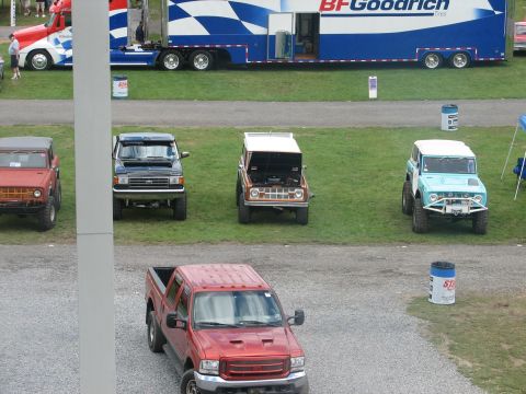 1992 Ford Bronco - A collection of vintage SUVs and a pickup truck are displayed outdoors, with a large semi-trailer in the background.