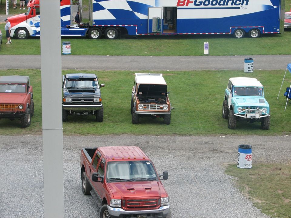 Row of early Ford Broncos on grass at a truck show with red Super Duty and BFGoodrich trailer