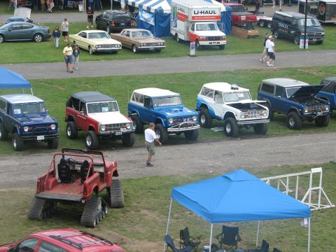 1992 Ford Bronco - Several Ford Broncos are displayed at an outdoor event, with one red and white model showing its engine.